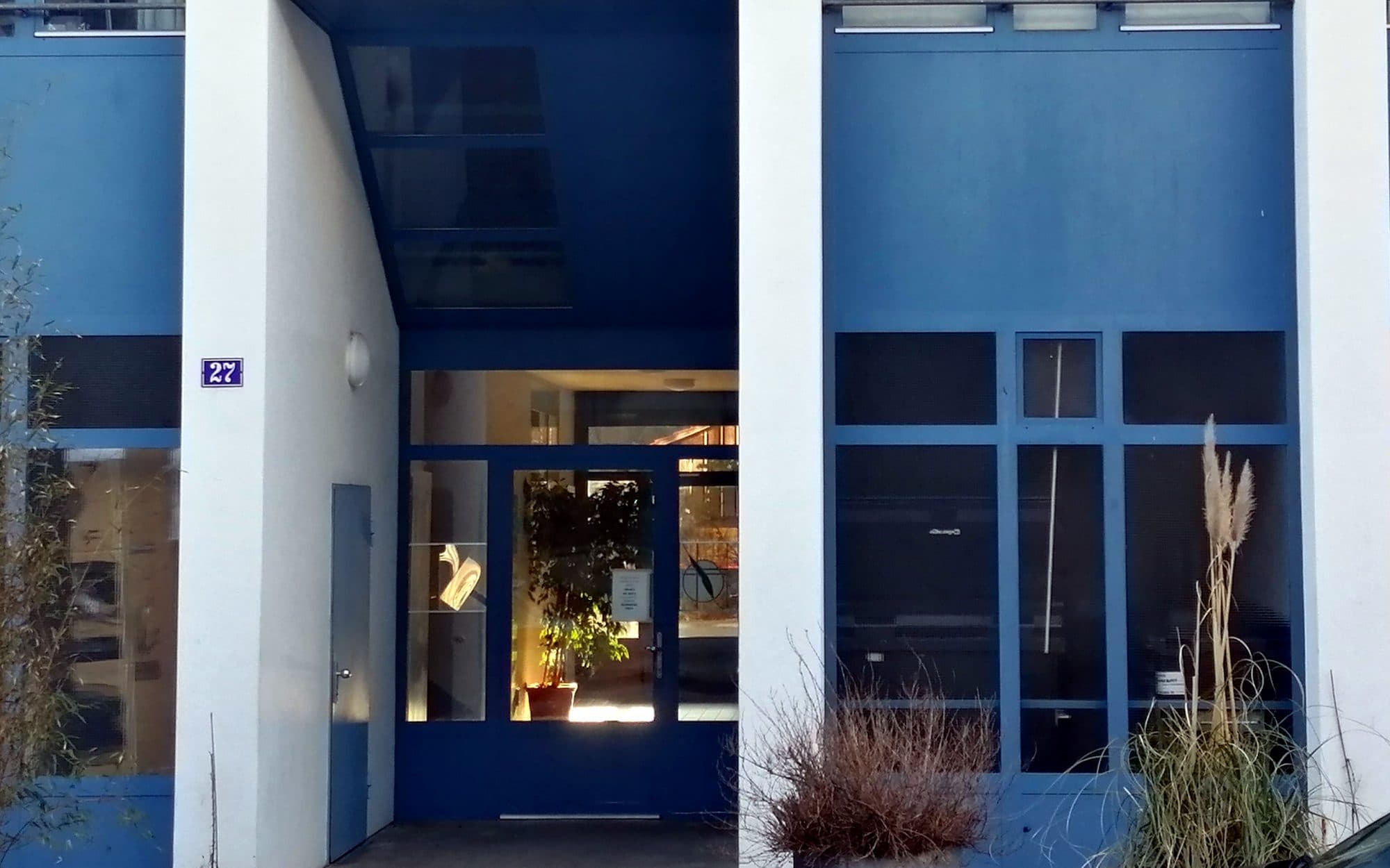 L'entrée de l'immeuble : porte vitrée bleue et plaque de rue portant le numéro 27